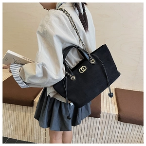 Detail of black suede tote bag featuring gold chain strap and iconic metal buckle