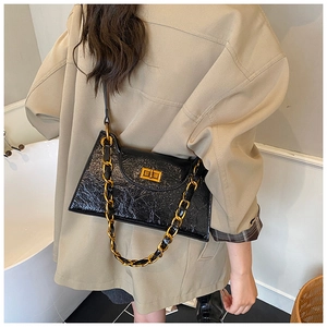 Detail of black wrinkled patent shoulder bag with gold chain and metal twist lock