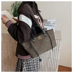 Detail of suede tote bag featuring golden double-ring buckle and elegant chain strap