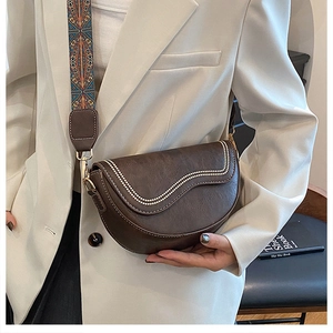 Detail of a dark brown half-moon saddle bag with vintage texture and ethnic woven strap