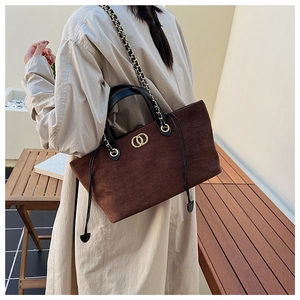 Detail view of brown faux suede tote bag featuring black leather handles and gold metal rings