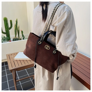Detail of dark brown suede tote bag featuring black leather handles and gold metal accents