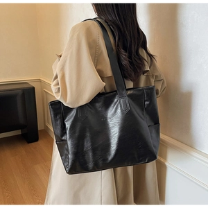 Detail of a large black leather tote bag with natural texture worn over the shoulder