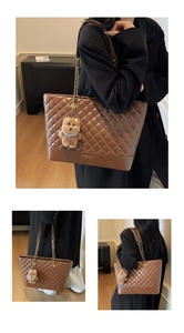 Detail of a brown quilted tote bag with gold logo lettering and a plush bear pendant charm