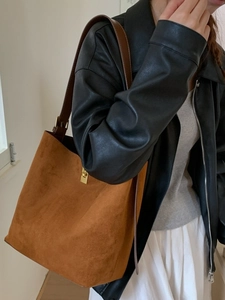 Brown vintage suede bucket bag with long leather strap and gold clasp on shoulder