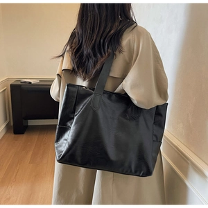 Close-up of black leather tote bag with subtle pebble texture and wide shoulder strap