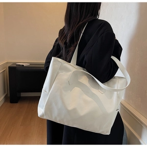 Detail shot of a spacious white shoulder bag with embossed logo on a fashion model