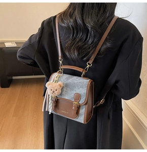 Détail d'un sac à dos bicolore avec pendentif ours porté sur une veste de costume