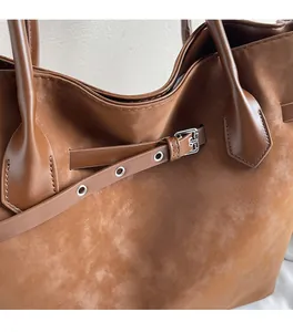 Close-up of brown faux leather tote bag with silver buckle strap and fine stitching details