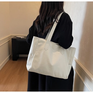 Side view of a white pebbled leather tote bag with long shoulder straps and side pockets