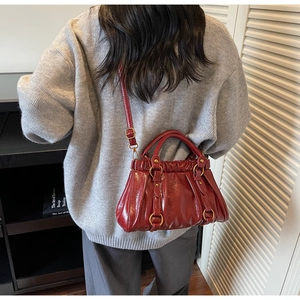 Detail of red glossy leather handbag with pleated design and adjustable shoulder strap