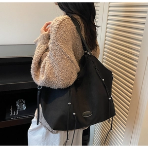 Detail view of large black tote bag with drawstring and metal bead on model shoulder