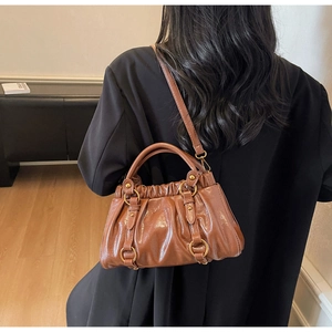 Brown ruched PU leather bag with gold hardware worn by a model in a minimal room