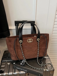 Brown suede tote bag with black handles and gold hardware on silver suitcase