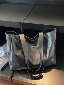 Minimalist large black tote bag with lychee texture and shoulder straps on a dark shelf