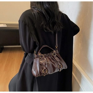 Detail of dark brown pleated leather handbag with golden ring buckles and metal rivets