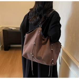 Detail of a large brown suede tote bag featuring silver beaded tassels and leather logo patch