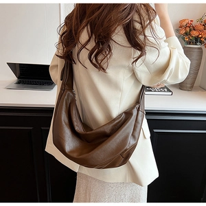 Detailed view of large dark brown leather hobo bag worn over shoulder on a beige blazer