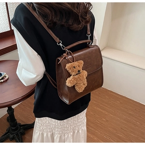 Close-up of vintage brown leather backpack with embossed detail and plush bear charm