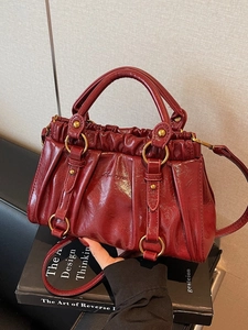 Deep red pleated cloud handbag with gold hardware displayed on books for commute