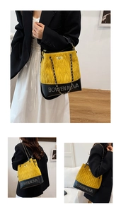 Detail of yellow quilted bucket bag with chain strap and contrast black leather base