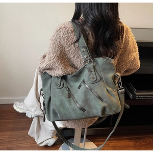 Close-up of a vintage green tote bag with silver rivets and zippers on soft faux leather