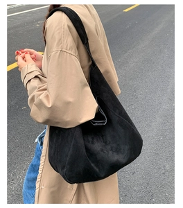 Macro view of a large black suede hobo bag with a wide shoulder strap in outdoor natural light