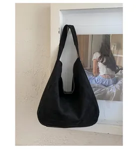 Detail of minimalist black suede hobo tote with wide shoulder strap on art wall