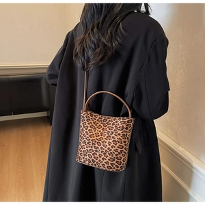 Sac seau léopard porté en bandoulière sur un long manteau noir pour un look d'hiver chic