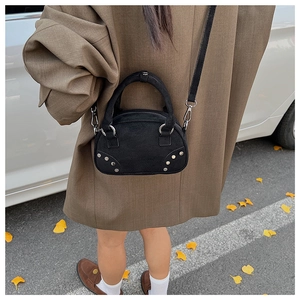 Detail of black suede mini bag showing silver studs and cross-body strap on model