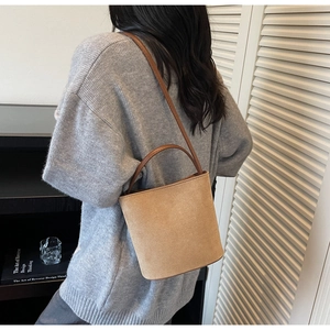Détail du sac seau en daim kaki avec poignée en cuir marron foncé porté sur un pull gris