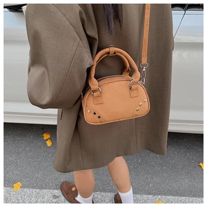 Outdoor shot of a tan suede crossbody bag with silver rivet details and shoulder strap