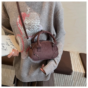 Detail of a dark brown suede crossbody bag featuring retro silver rivets and dual handles