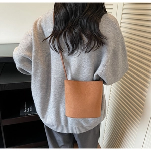 Gros plan du sac seau en daim marron caramel avec bandoulière sur un pull gris clair