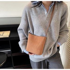 Gros plan du sac seau en daim marron au design minimaliste avec une bandoulière fine