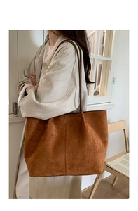 Detail of a large caramel suede tote bag featuring slim dark brown shoulder straps and a minimalist design