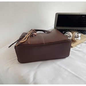 Detail of dark brown pebble leather tote bag featuring fine stitching and braided strap