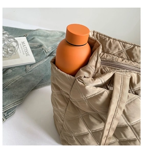 Quilted nylon tote bag in khaki next to a vibrant orange thermos on a white surface