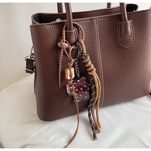 Close-up of a leopard print bear charm and braided lanyard on a brown tote bag handle