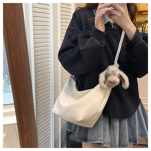 Detail view of white leather crescent tote with plush bunny charm and adjustable strap