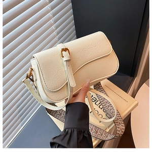 Détail d'un sac selle crème avec rabat ondulé, boucles dorées et bandoulière tissée
