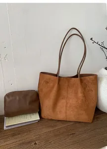Macro detail of brown frosted leather tote bag with matching zippered pouch on wood surface