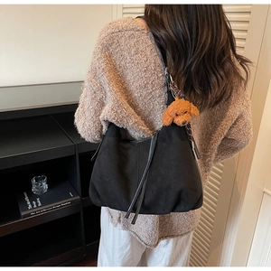 Detail of black suede hobo shoulder bag with fringe zipper and teddy bear charm