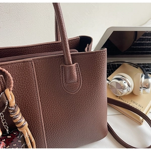 Detail of dark brown pebble leather tote bag with braided charm and zipper closure