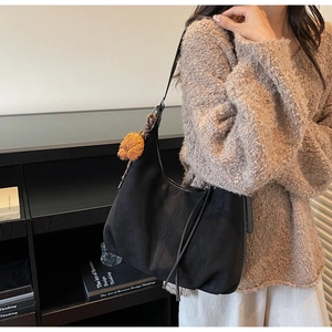 Detail of black suede hobo bag with long fringe tassels and cute plush poodle charm