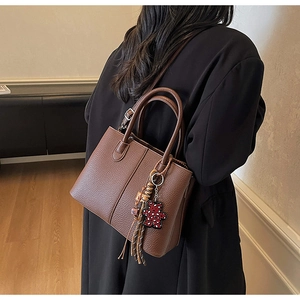 Rear view of model in black coat holding a brown leather tote bag with bear charm