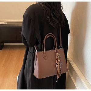 Detail of dark brown pebble leather tote bag featuring a decorative woven tassel charm