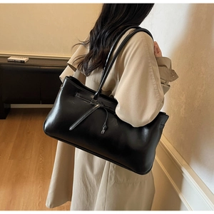 Detail of a large black tote bag with leather bow decoration worn by a model