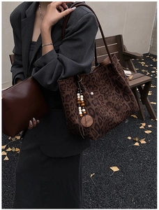 Dettaglio della borsa tote leopardata con ciondolo in legno e pochette su foglie autunnali