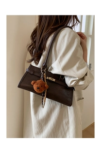 Detail of dark brown leather underarm bag featuring gold lock and cute bear charm